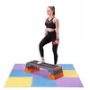 A woman is exercising on a step platform, holding a dumbbell. Voir les images du produit