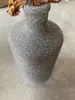 A close-up view of a textured gray vase with a dried brown leaf and stem inside. Produktbild-Vorschau