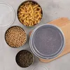 Several stainless steel food containers filled with different food items are arranged on a light gray surface, with a wooden cutting board visible. Produktbild-Vorschau