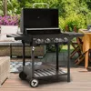 A black gas grill is set up on a wooden deck in a backyard setting, with outdoor furniture and plants visible. Produktbild-Vorschau