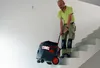 A man is pulling a vacuum cleaner down a set of stairs. Anteprima dell’immagine prodotto