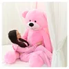 A woman is sitting on a bed, hugging a large pink teddy bear. Anteprima dell’immagine prodotto