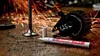 A paint marker and engine parts are on a wooden surface with sparks flying in the background. Produktbild-Vorschau