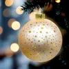 A close-up of a champagne-colored Christmas ornament with gold stars, hanging on a Christmas tree with blurred bokeh lights in the background. Náhled obrázku produktu