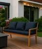 A wooden outdoor sofa with blue cushions sits on a wooden deck, with plants and a house in the background. Anteprima dell’immagine prodotto