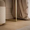 A close-up view of the base of a console table with a gold frame, next to a quilted ottoman and draped fabric. Produktbild-Vorschau