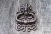 A close-up of an ornate, dark metal door knocker mounted on weathered wooden planks. Produktbild-Vorschau