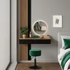 A modern bedroom vanity area with a floating desk, round illuminated mirror, and a green stool. Produktbild-Vorschau