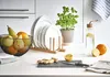A kitchen counter with various items including fruit, plates, a plant, and a water bottle. Produktbild-Vorschau