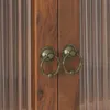 A close-up view of two ornate brass ring handles on a wooden cabinet door. Produktbild-Vorschau