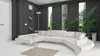 A modern living room with a large white sectional sofa, a small glass coffee table, and tall windows overlooking a garden. Náhľad obrázku produktu