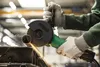 A person wearing work gloves is using an angle grinder to cut a metal pipe. Anteprima dell’immagine prodotto
