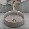A close-up, eye-level shot of a round, beige vessel sink with a gold faucet and drain. Náhľad obrázku produktu