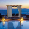 A pergola with gray curtains stands by a pool at sunset. Voir les images du produit