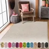 A shaggy cream rug is shown in a room with a chair, a pouf, and a cabinet. A row of color swatches is displayed below the rug. Produktbild-Vorschau