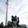 A black Maneki-Neko lucky cat figurine is placed in front of the Berlin TV Tower. Produktbild-Vorschau