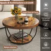 A round coffee table with a rustic wood finish and black metal legs, placed in a living room setting. The table has items on it and a lower shelf with books. Anteprima dell’immagine prodotto