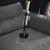 A person is using a cordless vacuum cleaner to clean a gray fabric sofa. Voir les images du produit