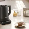 A Haier electric kettle is shown on a kitchen counter next to jars of sugar, a bag of coffee, and a cup of coffee. Podgląd zdjęcia produktu