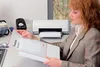 A woman is looking at a document in front of a printer. Produktbild-Vorschau