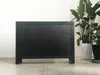 A black sideboard is shown against a white wall with plants in pots to the right. Produktbild-Vorschau