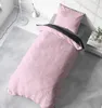 A pink duvet cover and pillow set is laid out on a bed with a grey rug and a floor lamp in the background. Produktbild-Vorschau