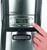 A close-up of a coffee maker's control panel with a finger pressing a button. Produktbild-Vorschau