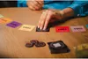 A person's hand is playing a card game on a wooden table. Anteprima dell’immagine prodotto
