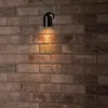A black outdoor wall light is mounted on a brick wall, casting a warm glow downwards. Produktbild-Vorschau