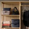 Storage baskets and folded sweaters on shelves, with a handbag and clothes on hangers in a closet. Produktbild-Vorschau