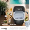 An ice maker is displayed on a wooden table next to drinks, fruit, and ice cubes, with a swimming pool in the background. Náhled obrázku produktu