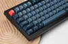 A close-up view of a black mechanical keyboard with dark gray and red keycaps, resting on a wooden surface. Produktbild-Vorschau
