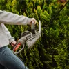 A person is using a hedge trimmer on a green bush. Voir les images du produit