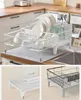 A white dish drying rack filled with plates, bowls, cups, and cutlery, placed on a kitchen counter next to a sink. Two smaller inset images show a stack of white containers and a black dish drying rack. Produktbild-Vorschau
