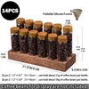 A set of 14 glass jars with wooden lids, filled with coffee beans, arranged on a wooden stand. A foldable silicone funnel is shown in the top right corner. Produktbild-Vorschau