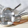 A collection of stainless steel cookware, including pots and pans, arranged on a table with a neutral background. Podgląd zdjęcia produktu
