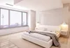A modern bedroom with a large window overlooking a city skyline. Produktbild-Vorschau