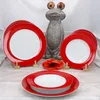 A set of red and white plates arranged on a table with a decorative frog statue and a red flower in the background. Produktbild-Vorschau