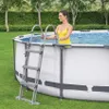 A woman in a yellow swimsuit is standing in an above-ground swimming pool, holding onto the ladder. Produktbild-Vorschau