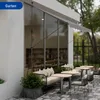 An outdoor seating area of a cafe or restaurant with tables, chairs, and a sofa, featuring a retractable awning. Anteprima dell’immagine prodotto