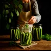 A person is adding herbs to jars of pickles. Produktbild-Vorschau