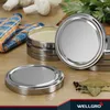 A collection of silver jar lids and a stack of jars with yellow contents, along with some bay leaves and peppercorns, arranged on a wooden surface. Produktbild-Vorschau