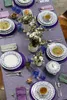 A beautifully set dining table with floral patterned plates, cutlery, glasses, and floral arrangements. Produktbild-Vorschau