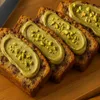 Bananenbrot Scheiben mit Pistaziencreme bestrichen und gehackten Pistazien bestreut auf Holzteller Produktbild-Vorschau