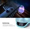 A baby sleeping in a crib next to a humidifier with colorful lights. Produktbild-Vorschau
