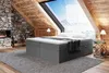 A bedroom scene in a rustic attic with a large window overlooking a snowy mountain landscape. The bed is the central focus, with a fireplace on the left and a side table on the right. Produktbild-Vorschau