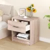 A light wood nightstand with an open drawer, placed next to a bed. There are books and glasses on the shelf, and a vase with sunflowers on top. Podgląd zdjęcia produktu