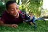 A young boy is lying on the grass, playing with a dinosaur toy. Produktbild-Vorschau