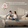A family is sitting on a couch in a living room, with a photo frame collage on the wall behind them. Produktbild-Vorschau