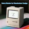 A retro-style computer alarm clock with a pixelated smiley face on its screen, placed on a surface with rainbow stripes. Produktbild-Vorschau